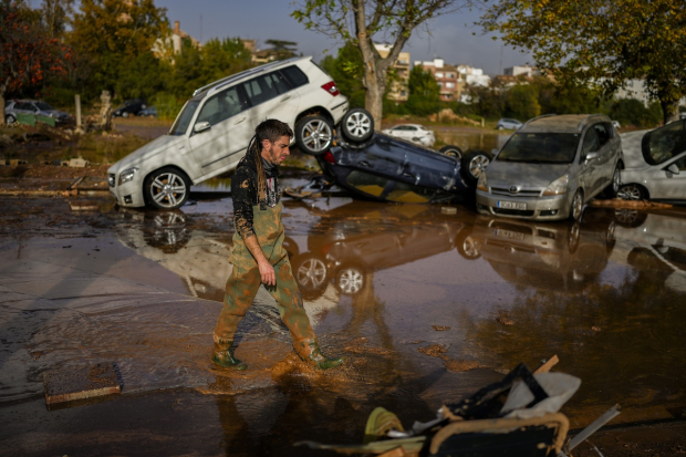 Un ciudadano camina frente a una pila de autos arrastrados por el fuerte nivel de lluvia e inundaciones.